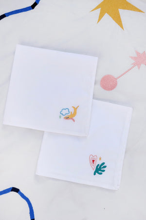The first napkin has a yellow fish with the blue outline of a cloud, and the second has a pink and red heart and green filled in leaf embroidered.
