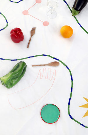 A close up image of the tablecloth, showing the green and blue embroidered swirl, and the pale pink hand. 