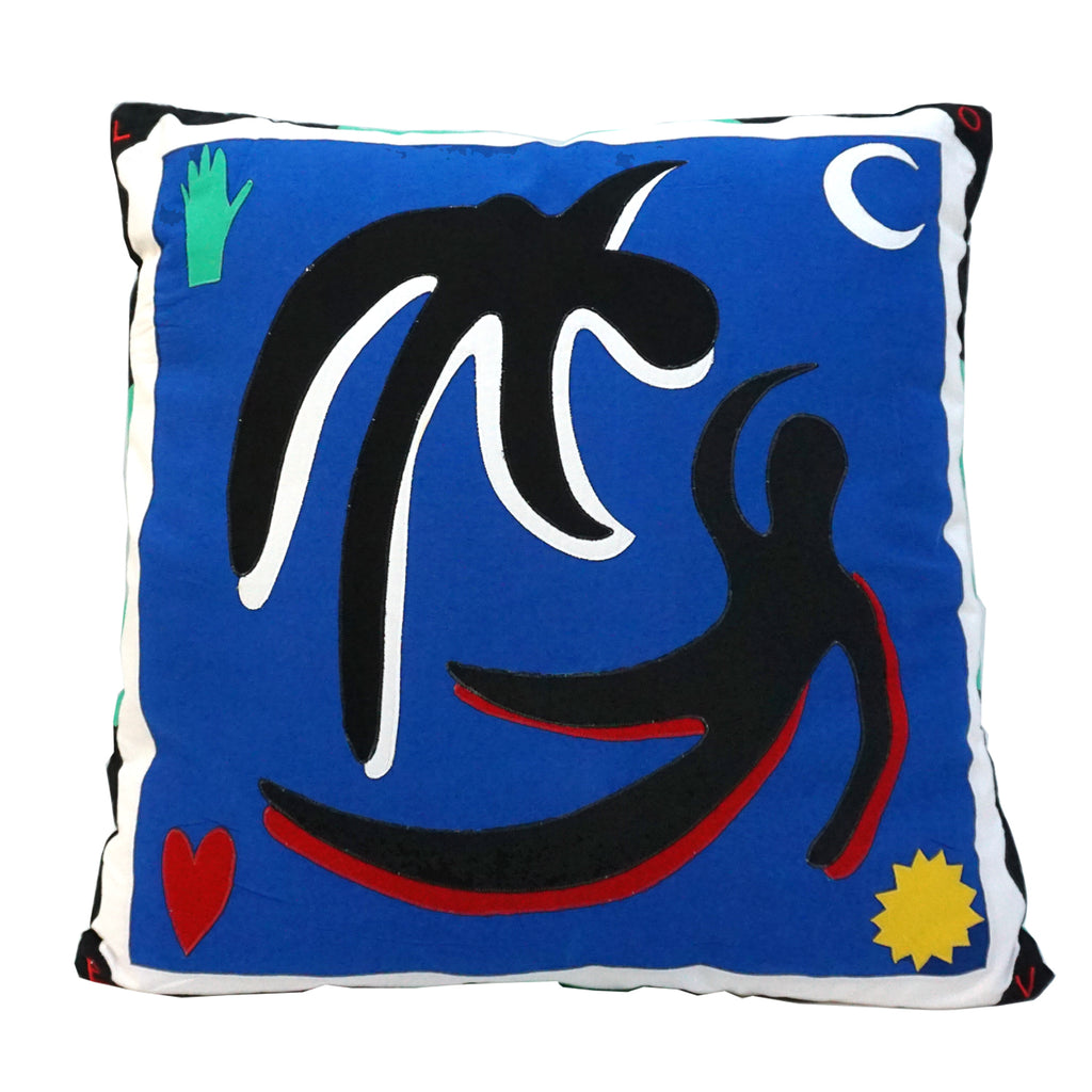 Cushion with a dark blue background and white and black border. The design shows two figures floating - with black, white and red fabric. In the top left corner is a green hand, bottom left a red heart, top right a white crescent moon and bottom right a yellow star. 