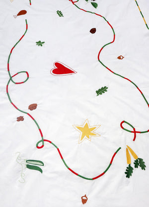 The white tablecloth has Christmas themed items embroidered on it: red heart, green leaves, green beans, carrots, chicken/turkey drumstick, a bright star and a red and green swirl covering the entire middle section.