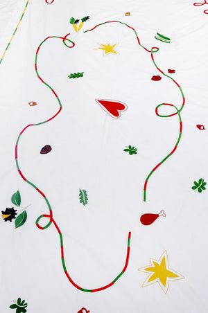 The white tablecloth has Christmas themed items embroidered on it: red heart, green leaves, green beans, carrots, chesnuts, chicken/turkey drumstick, a bright star and a red and green swirl covering the entire middle section.